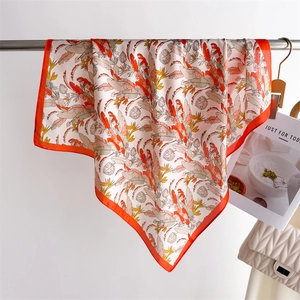 Detail of tropical leaf print silk scarf with vibrant orange border hung on metal rack