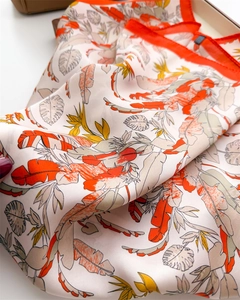 Detailed view of silk scarf with tropical leaf prints and vibrant orange hem finish