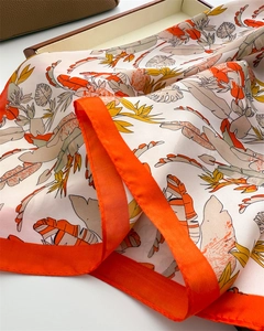 Detail of silk scarf with tropical leaf prints and bright orange border on a leather bag