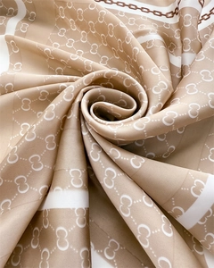 Macro shot of silk scarf showing glossy interlocking chain pattern and beige fabric texture