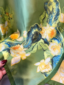 Detail of silk satin scarf showing glossy emerald fabric with artistic lotus patterns