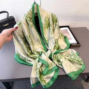 Floral print silk scarf in green and beige draped with a stylish handbag background
