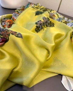 Dettaglio della sciarpa in seta gialla con stampe floreali e consistenza morbida e lucida