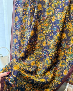 Texture détaillée de l'écharpe en soie bleu marine avec motif paisley et bordure rouge