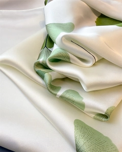 Gros plan détaillé d'une écharpe en satin crème avec motif ginkgo vert et texture soyeuse