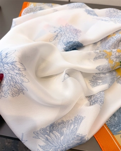 Close-up of lightweight silk scarf featuring blue floral prints and orange contrast borders