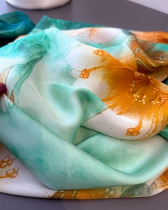 Close-up of silk scarf fabric showing elegant green and orange floral print patterns