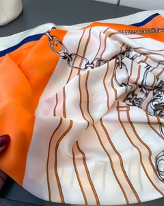 Detail of silk satin scarf with orange geometric stripes and metal chain print