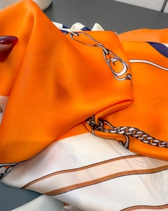 Detail of luxury silk scarf with orange chain print and metal buckle pattern