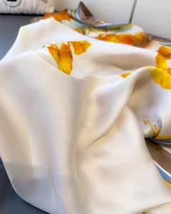 Detailed macro view of yellow floral patterns on pearl white silk satin scarf fabric