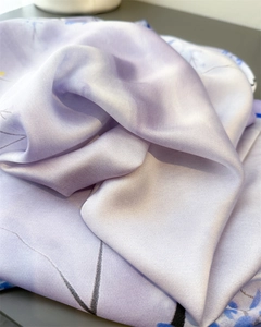Close-up of lavender silk scarf featuring blue floral prints and smooth satin texture