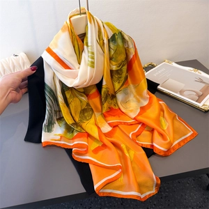 Floral print lightweight silk satin scarf in orange and yellow draped over dark clothing