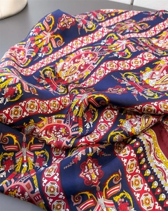 Détail macro du foulard en soie bleu marine aux motifs baroques dorés et bords rouges