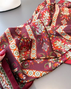 Gros plan d'une écharpe en soie avec motifs paisley rouge foncé et motifs géométriques