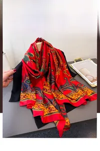 Detail eines roten Seidenschals mit goldenem Paisleymuster und dunkelblauem Saum