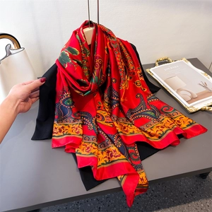 Roter Seidenschal mit Pfauen-Paisley-Muster, elegant auf dunkler Kleidung drapiert