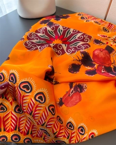 Detail eines leuchtend orangefarbenen Seidenschals mit Mandala- und Pfauenfeder-Prints