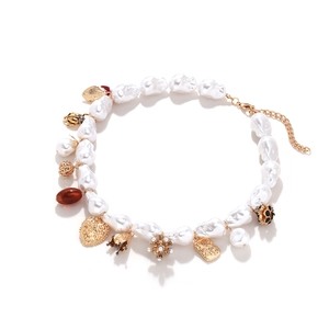 Collier de perles baroques avec pendentifs cœur et fleur dorés sur fond blanc