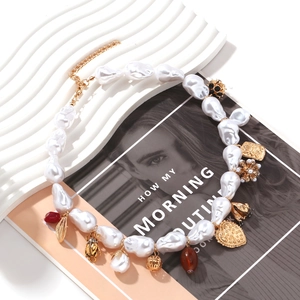 Détails d'un collier en perles baroques avec scarabée doré, cœurs et pendentifs fleurs