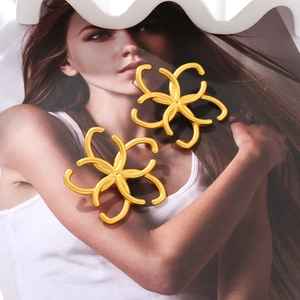 Macro detail of gold flower earrings with a matte finish and openwork hollow design