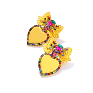 Dettaglio di orecchini a cuore dorati con cristalli colorati e raffinato fiocco vintage