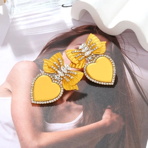 Orecchini vintage a cuore dorato con fiocco di strass su sfondo di rivista di moda