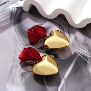 Detail of red satin rose and gold heart drop earrings on a stylish magazine background