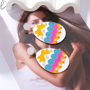 Detail view of colorful enamel Easter egg earrings with bow patterns and pearl accents