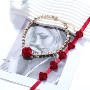 Détail du collier chaîne dorée serti de cristaux avec une fleur de rose en tissu rouge