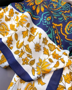 Close-up of paisley pattern and floral motifs on a navy and yellow silk-feel scarf