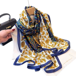 Floral paisley silk scarf in blue and yellow draped over a white knit top with a handbag