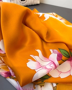 Detailed close-up of orange silk scarf showing vibrant floral patterns and silky texture