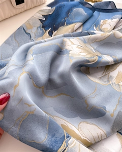Détail d'un foulard en soie avec de grandes fleurs blanches et bordures dorées sur bleu