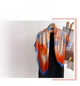 Detail of silk-like floral square scarf with blue rolled edges and vibrant orange print