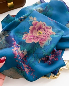 Close-up of silk scarf with pink peony floral patterns on peacock blue fabric
