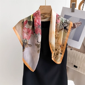 Silk-like floral scarf with beige base and orange border hung on wooden hanger