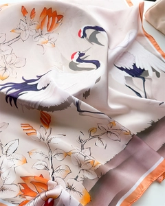 Dettaglio della stampa con gru e fiori su un foulard di raso con eleganti bordi arancioni