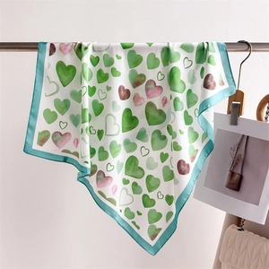 Elegante foulard in seta bianca con cuori verdi appeso accanto a una borsa beige trapuntata