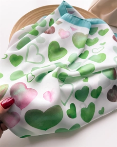 Dettaglio di un foulard di seta con cuori verdi e rosa che mostra la texture soffice e leggera