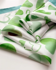 Dettaglio ravvicinato della trama in seta e stampa a cuori sul foulard verde e bianco