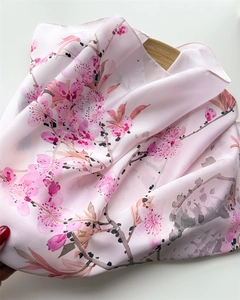 Detail of pink silk-like scarf with floral ink print on a white tabletop background