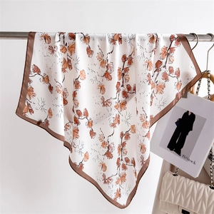 Detail of silk satin scarf with orange ginkgo leaf print and brown borders on display