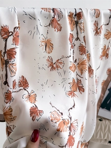 Close-up of silk-like satin fabric with orange abstract floral print and soft drapes