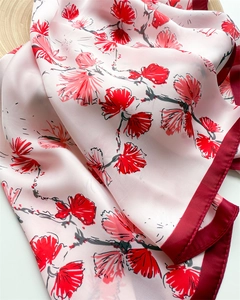 Close-up of floral silk scarf showing vibrant red flowers on pink fabric with fine stitching