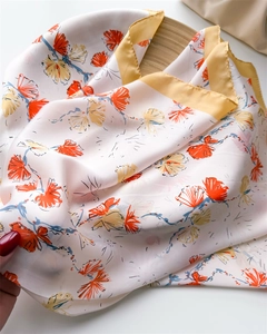 Close-up of a floral silk-like scarf with orange petals and a bright yellow border