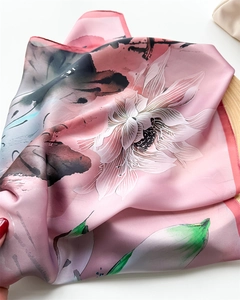 Détail d'un foulard en soie rose à motif lotus plié sur un plateau en bois