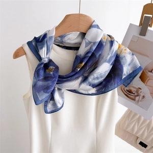 Close-up of blue floral silk scarf tied on a white dress with a quilted handbag