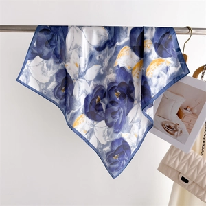 Detail of silk square scarf with blue floral print hanging next to a quilted beige bag