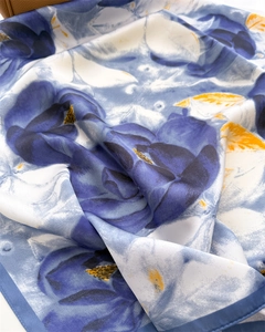 Close-up of blue floral print silk scarf featuring yellow leaves and glossy fabric texture