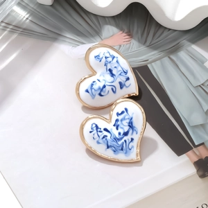 Detail of blue and white heart earrings with gold trim on a decorative magazine surface